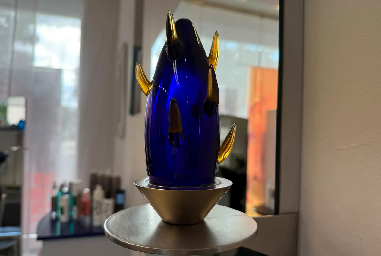 Blaue Glasskulptur mit goldenen Spitzen auf einer Ablage im Salon.